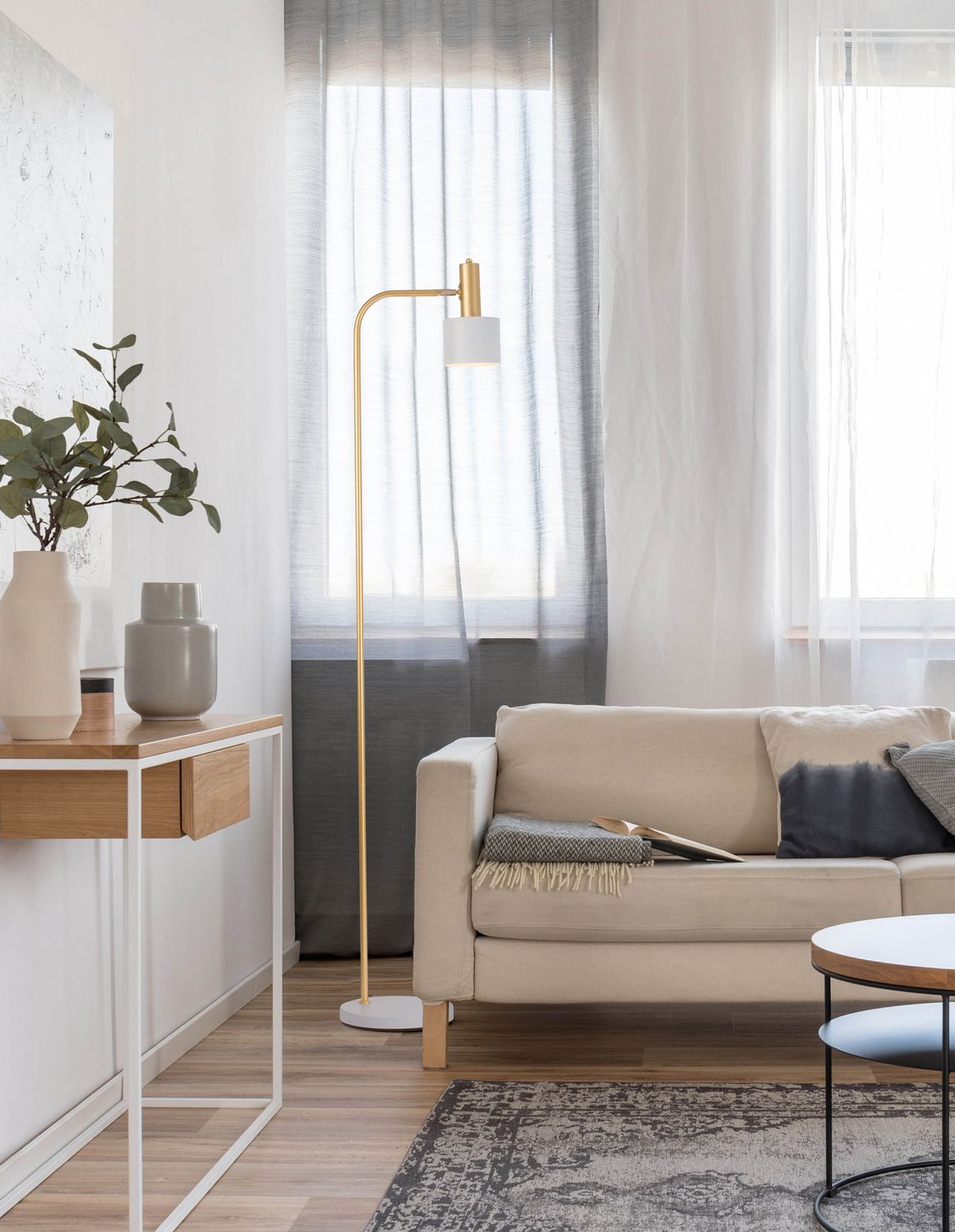 Lampadaire doré allumé dans un salon contemporain près d'un canapé beige et de rideaux.
