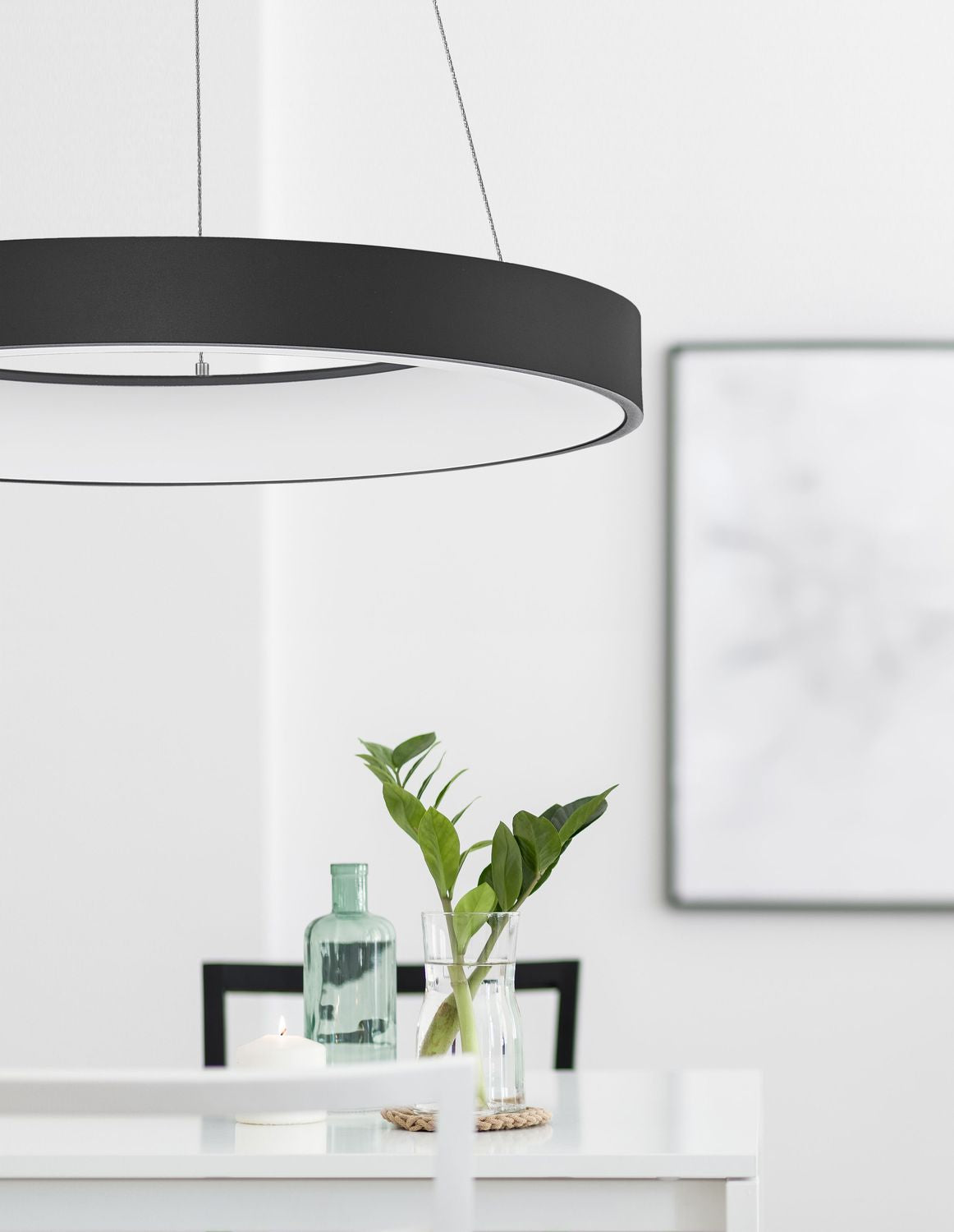 Suspension noire allumée au-dessus d'une table blanche avec plantes et bougie