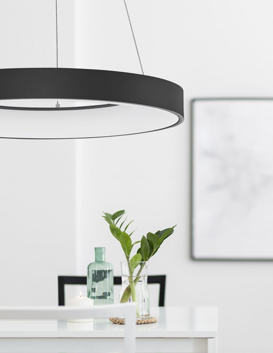 Suspension noire allumée au-dessus d'une table blanche avec plantes et bougie
