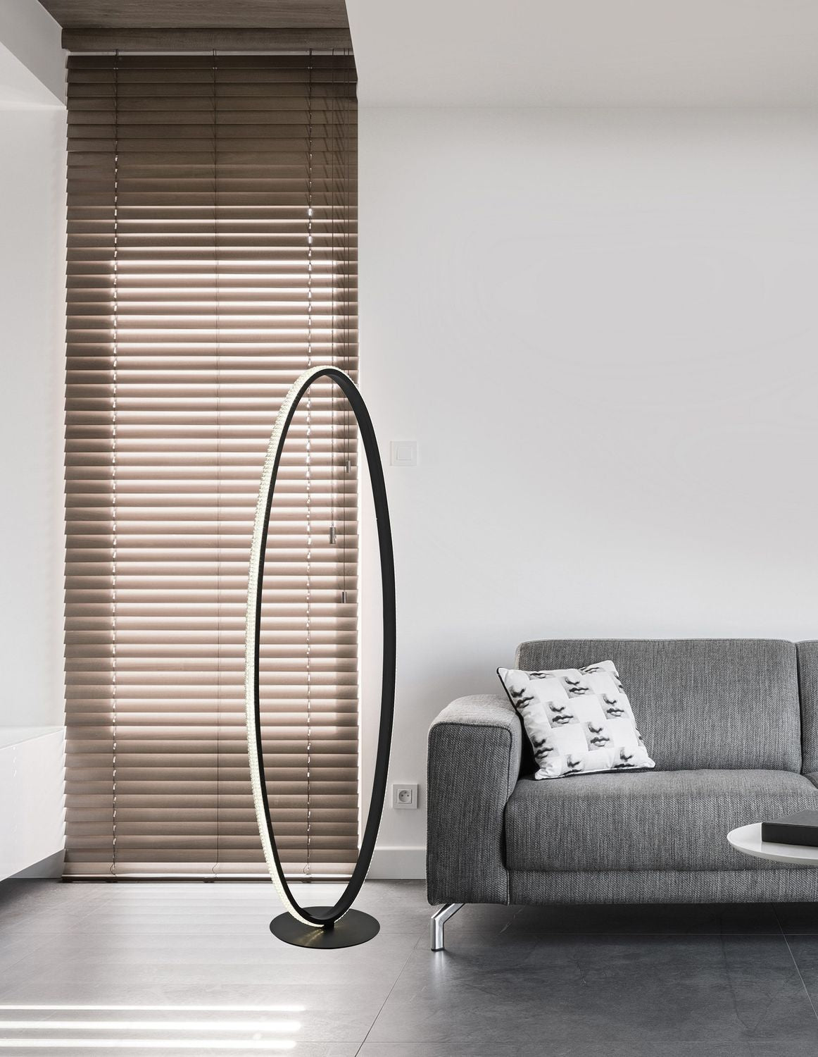 Photo d'ambiance : lampadaire ovale noir allumé devant stores et canapé gris.