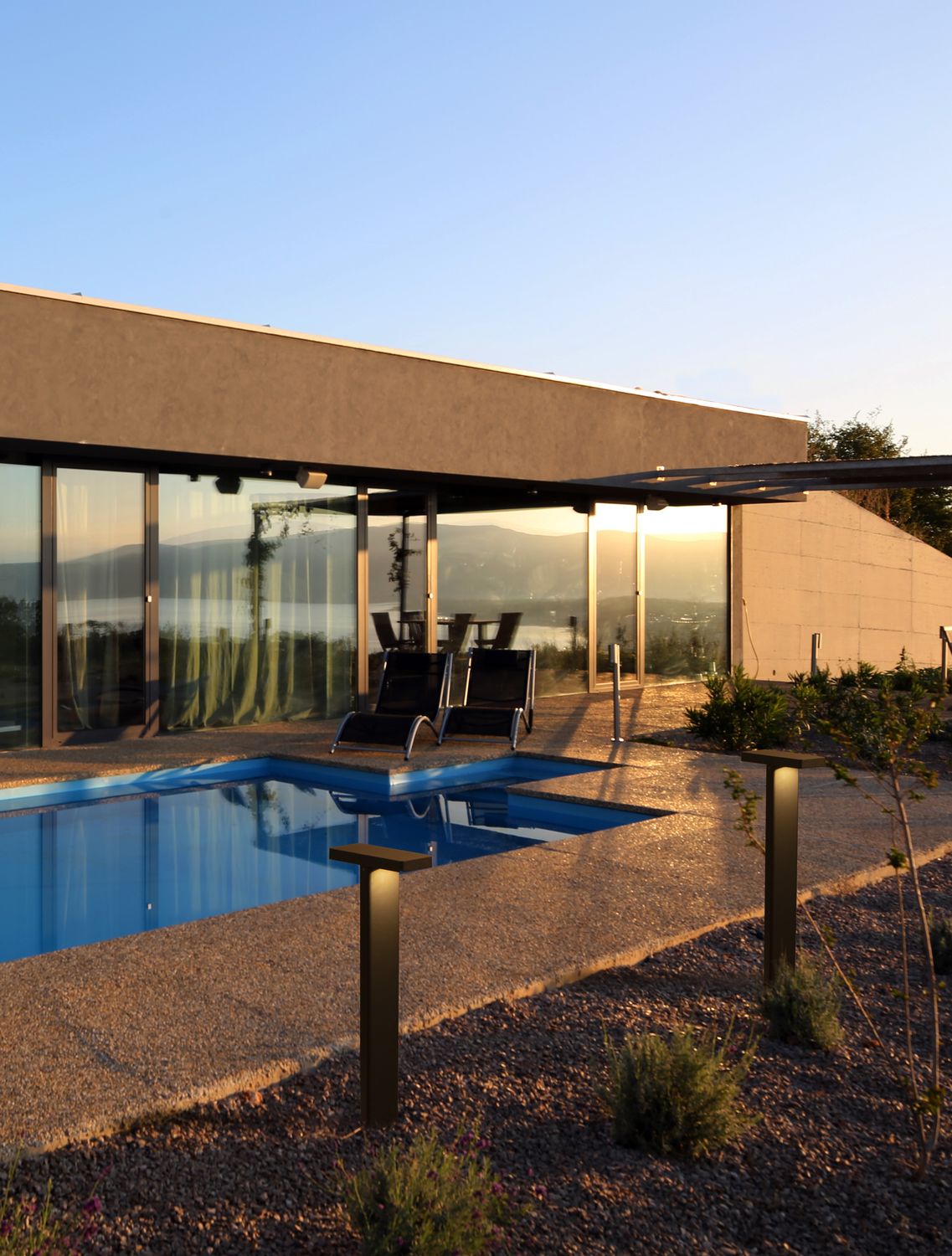 Borne anthracite dressée au bord d'une piscine, terrasse et baies vitrées au coucher du soleil.
