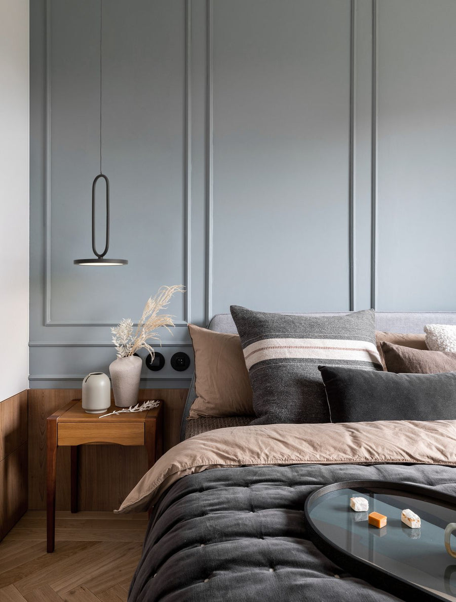 Suspension noire allumée au-dessus d'une table de chevet dans une chambre bleu-gris