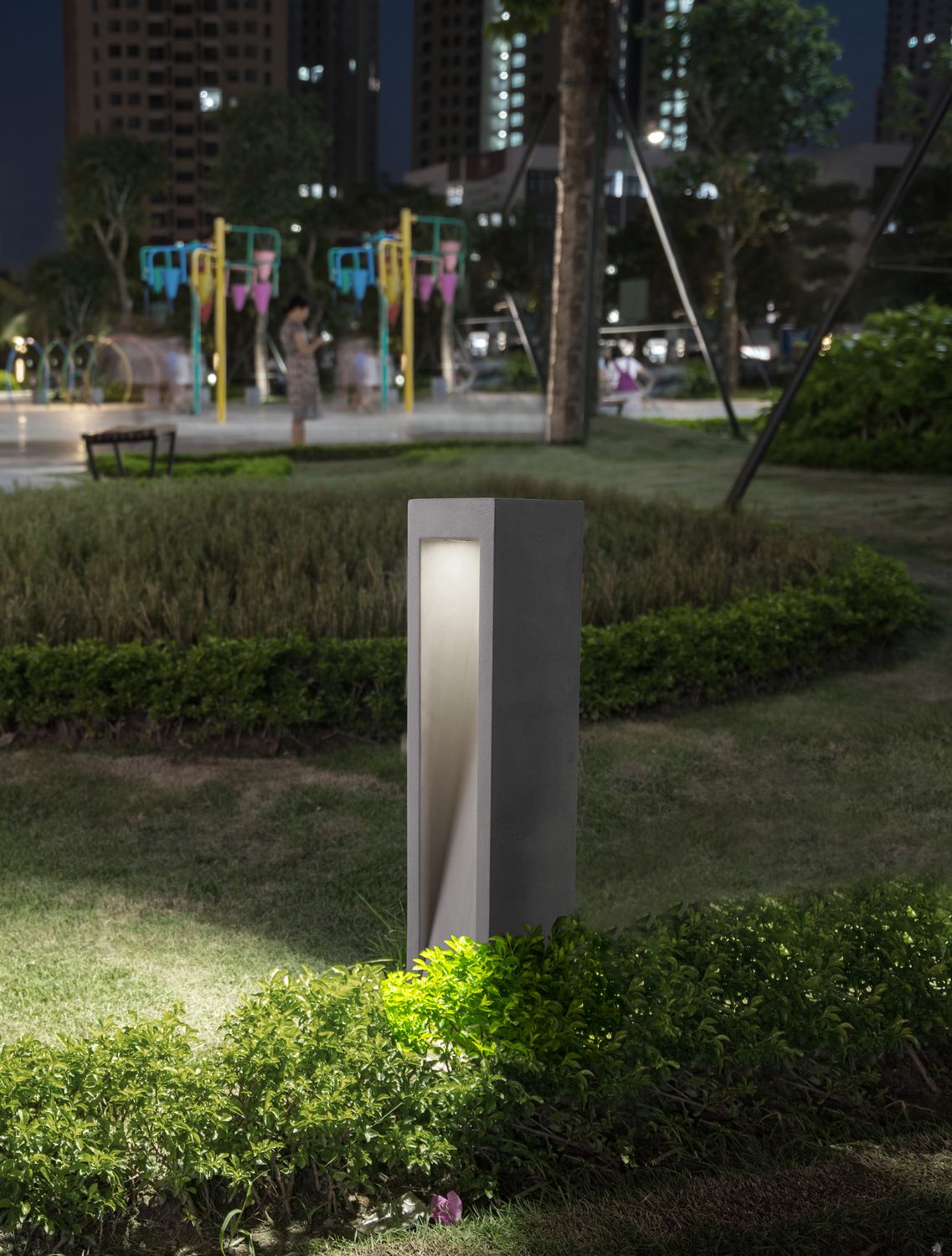 Borne lumineuse grise éclairée dans un jardin la nuit près d'une aire de jeux