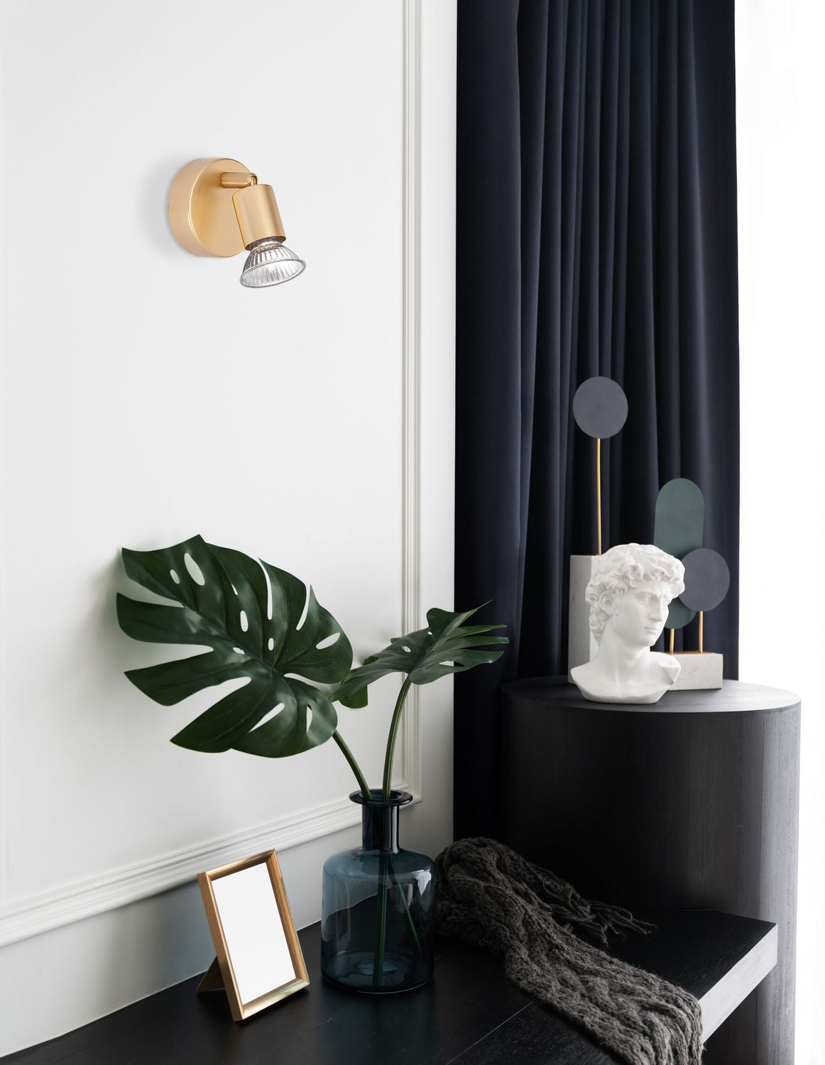 Applique dorée fixée sur mur blanc, ambiance déco avec plante verte et rideau sombre