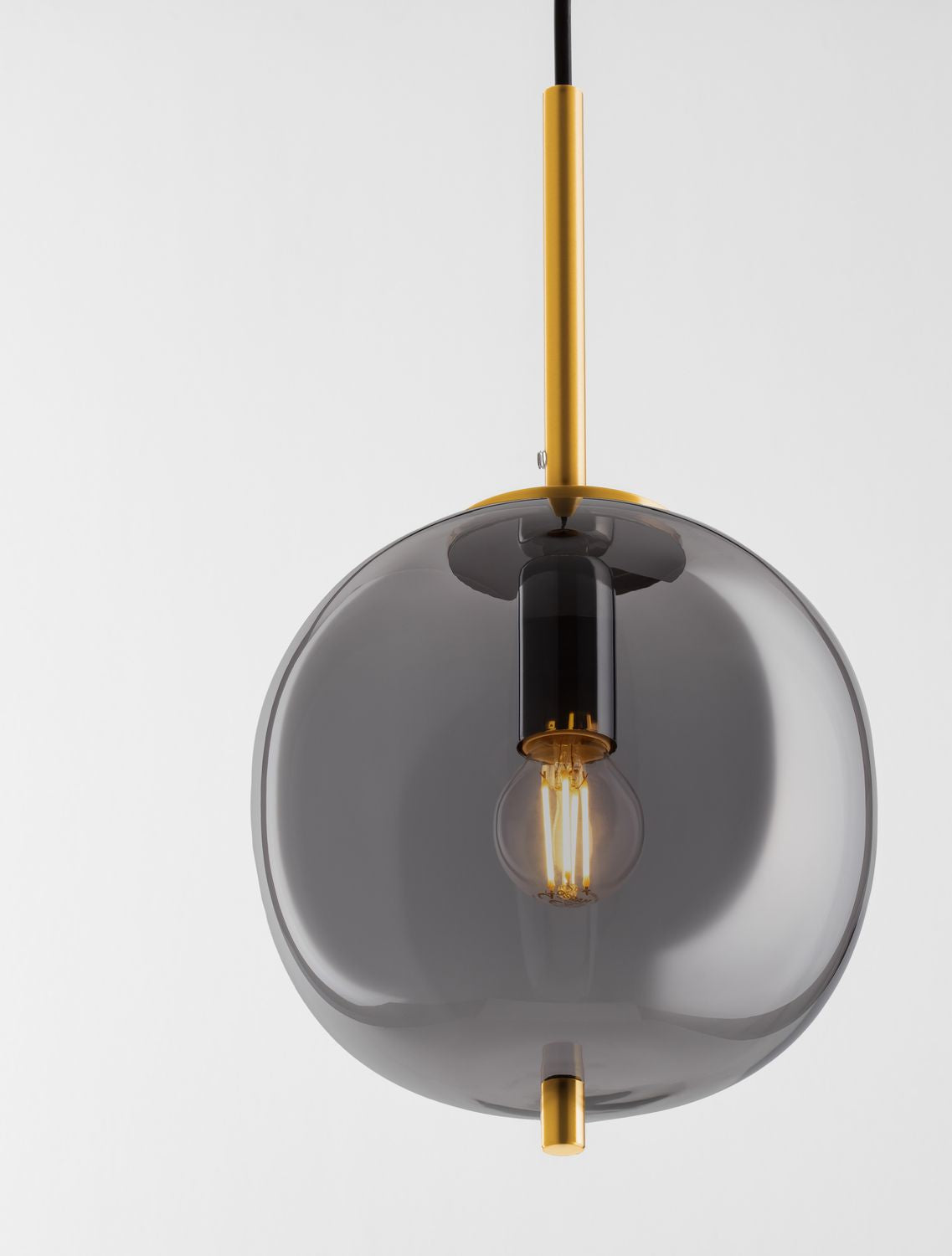 Vue rapprochée de la suspension en verre fumé, mettant en valeur la douille et l'ampoule dorée.