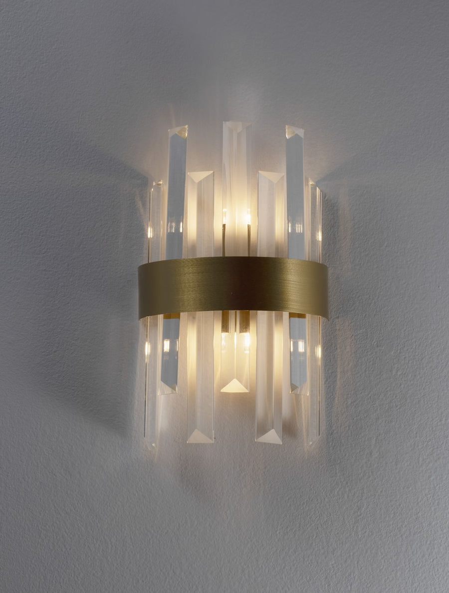 Applique allumée sur mur gris, halo de lumière chaude diffusée par les prismes