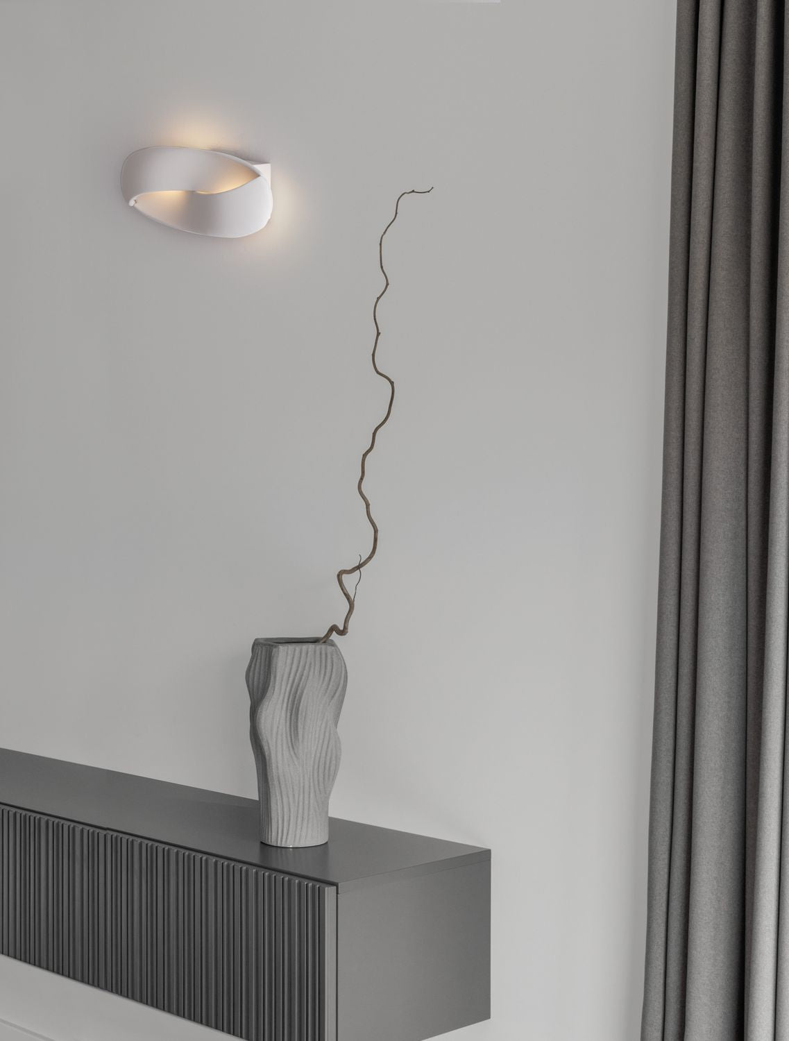 Applique murale blanche allumée, fixée sur un mur gris dans un intérieur épuré