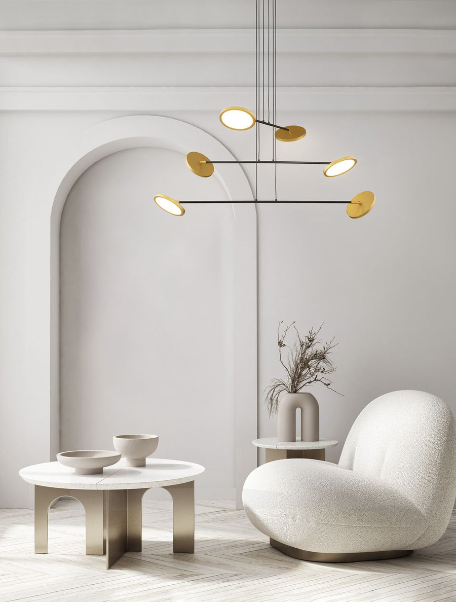 Suspension dorée et noire installée dans un salon blanc, au-dessus d'une table basse.
