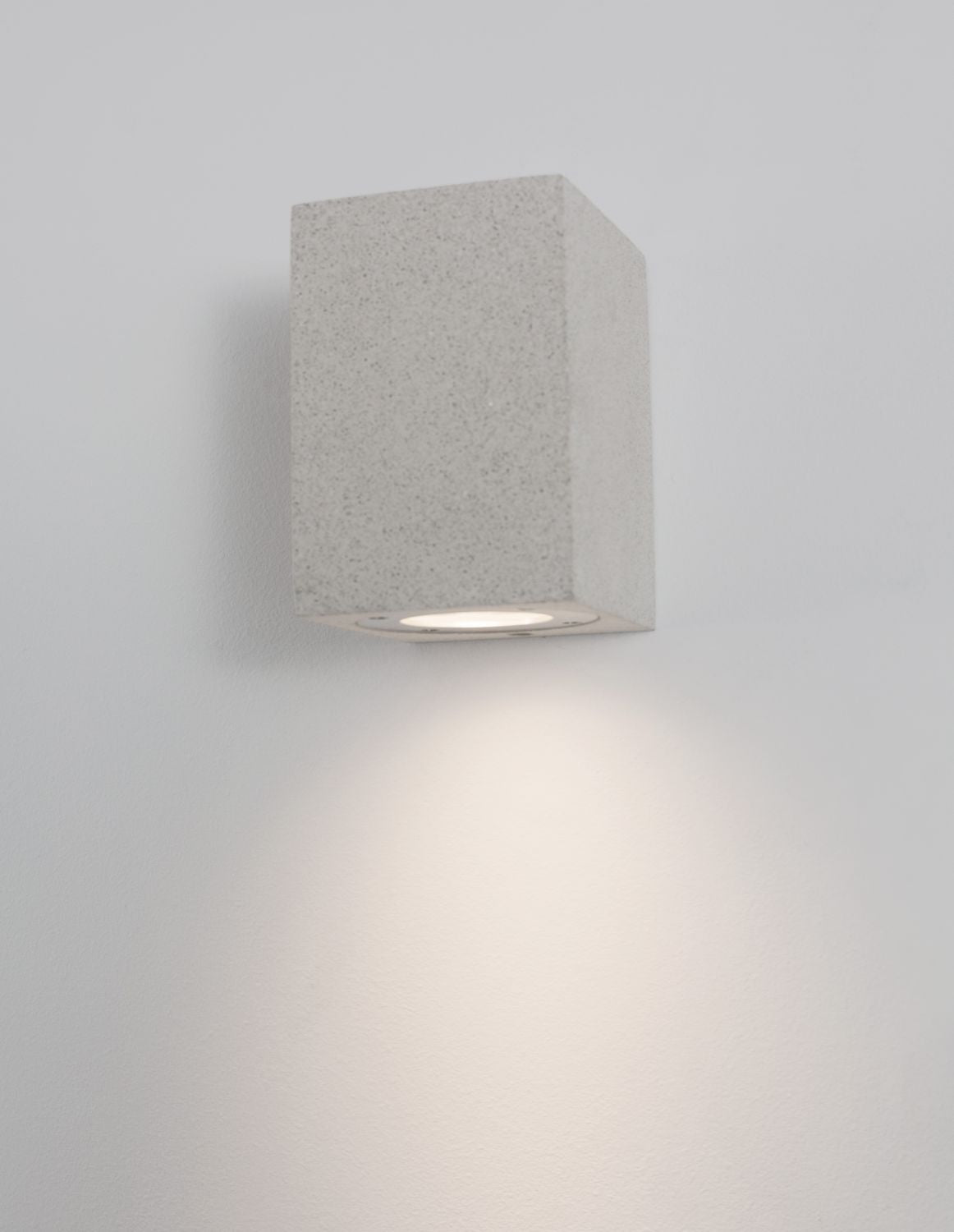 Applique murale blanche allumée sur mur clair, halo lumineux diffus vers le bas