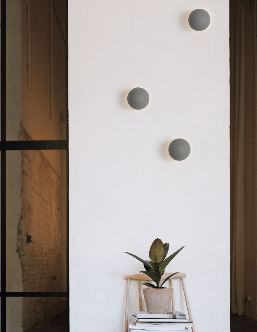 Trois appliques murales grises allumées sur un mur blanc en intérieur.