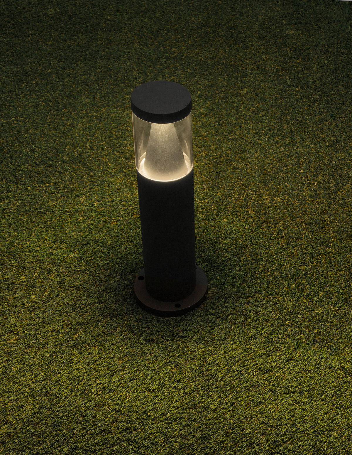 Borne lumineuse noire allumée, installée sur gazon synthétique, vue de trois quarts