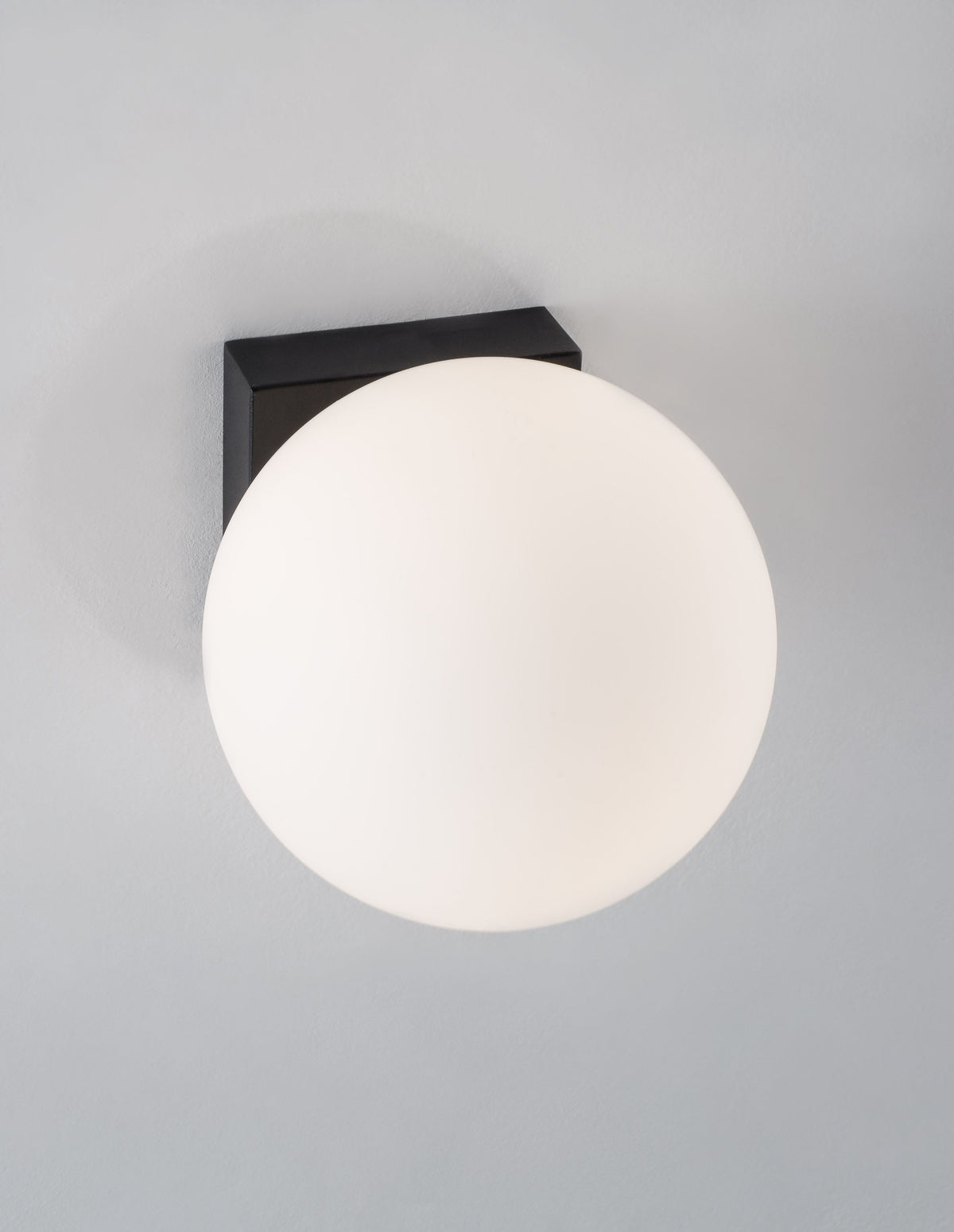 Applique murale noire fixée au mur, avec globe en verre blanc.