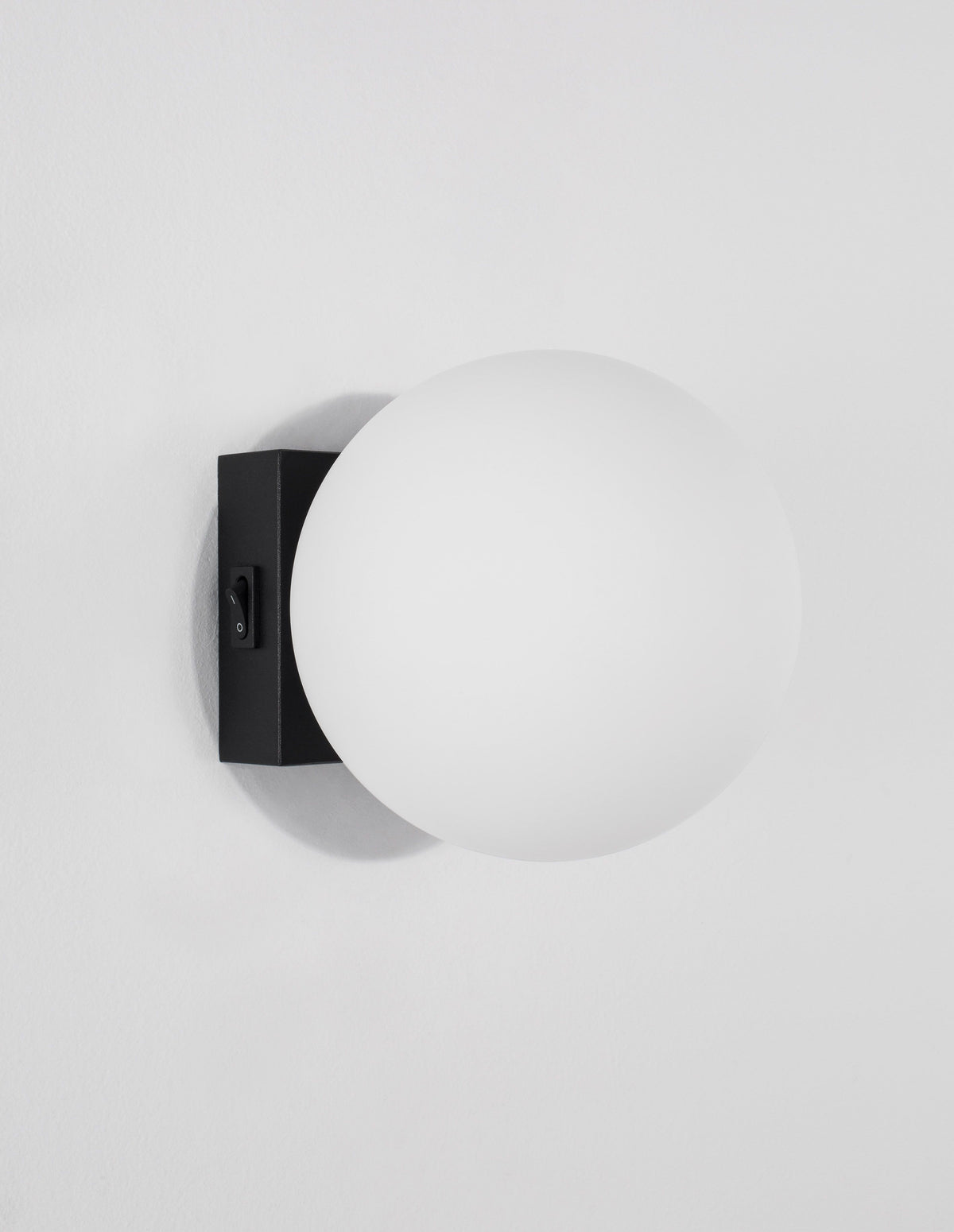 Profil de l'applique murale noire avec son interrupteur, globe blanc et ombre portée.