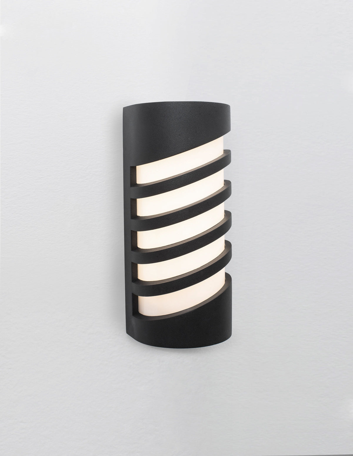Luminaire allumé de face, lumière chaude traversant le diffuseur entre les lames.