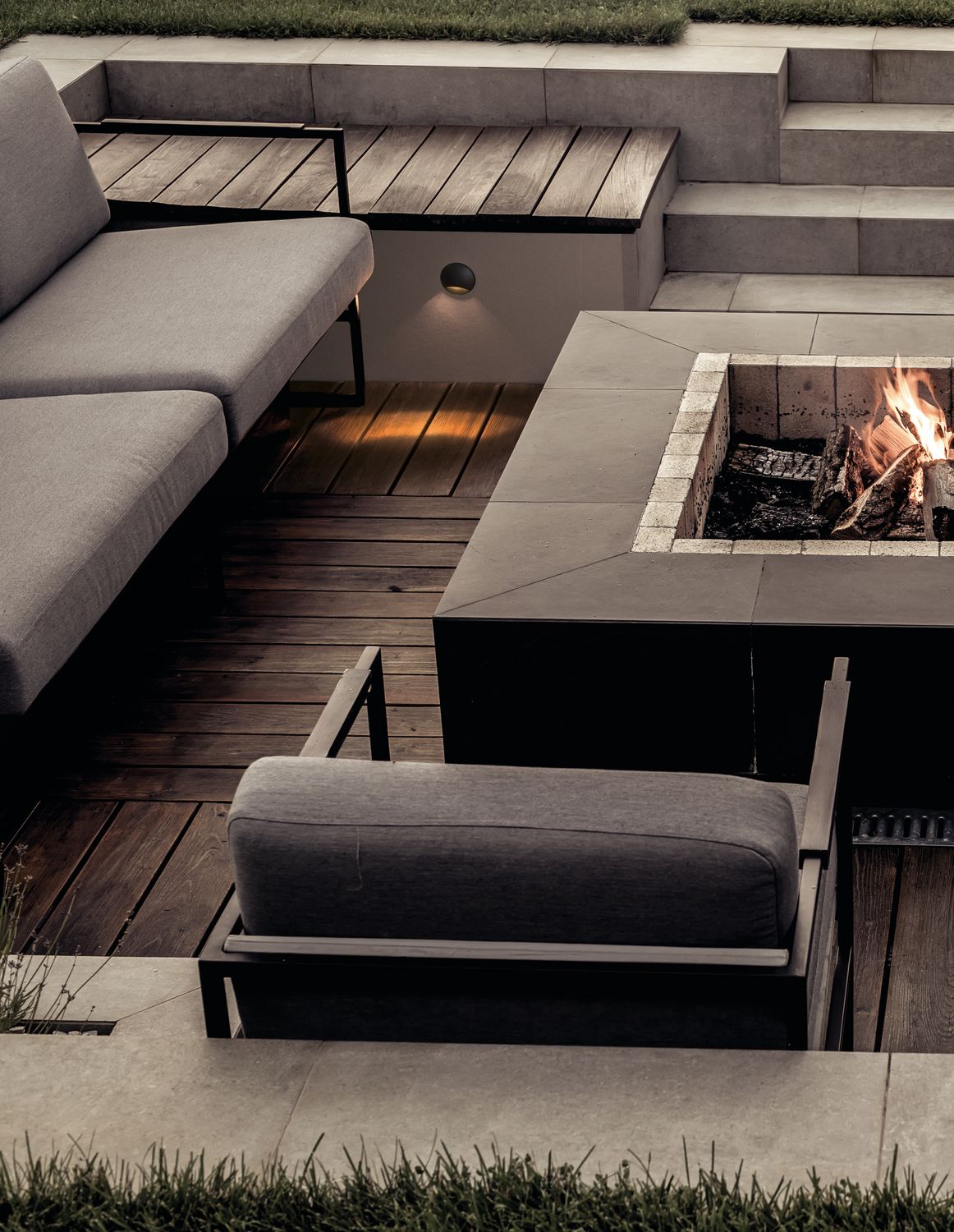 Mise en ambiance nocturne sur une terrasse en bois avec canapé et foyer extérieur