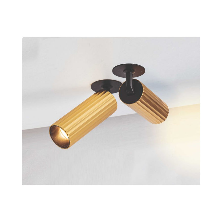 Deux spots dorés nervurés orientables fixés au plafond, diffusant une lumière chaude sur le mur.