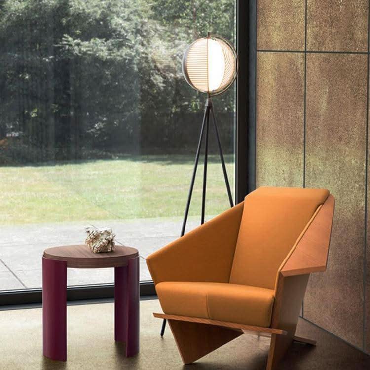 Mise en ambiance salon : lampadaire trépied allumé près d'un fauteuil orange et baie vitrée