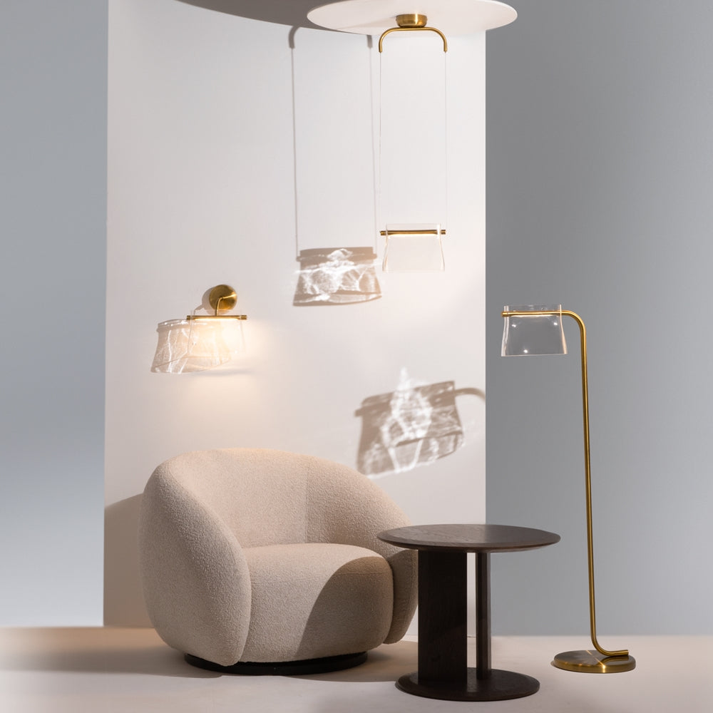Mise en ambiance avec lampadaire, suspension et applique dorés près d'un fauteuil