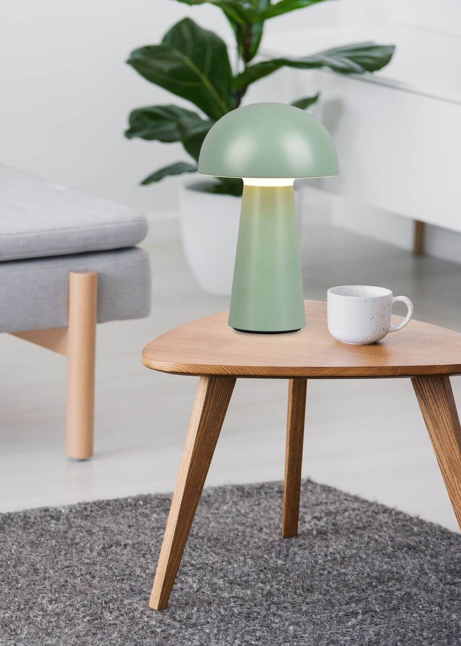 Vue rapprochée de la lampe verte allumée sur une table en bois clair.