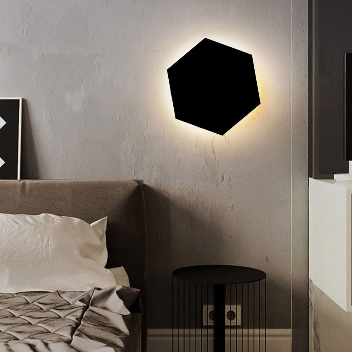 Applique hexagonale noire fixée au mur près d'un lit, lumière indirecte chaude soulignant la silhouette.