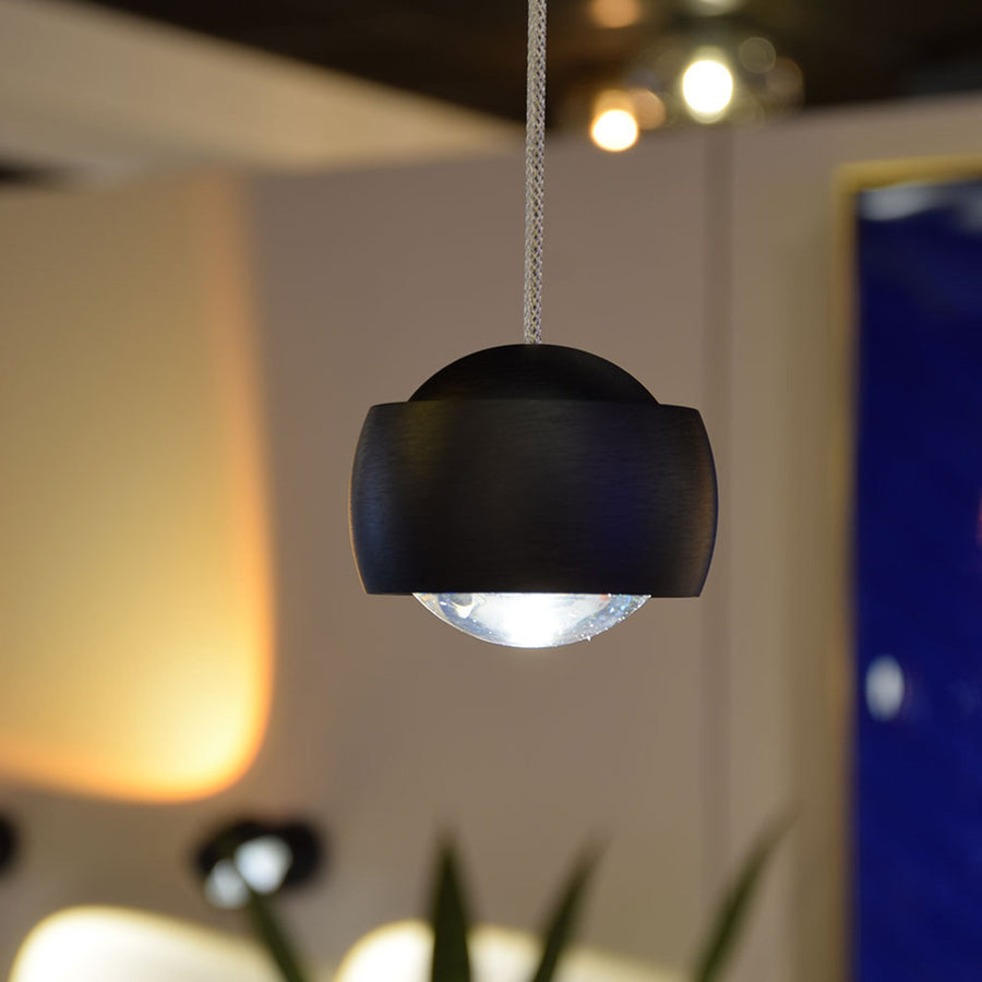 Détail d'une suspension noire avec diffuseur en verre transparent et câble tressé.