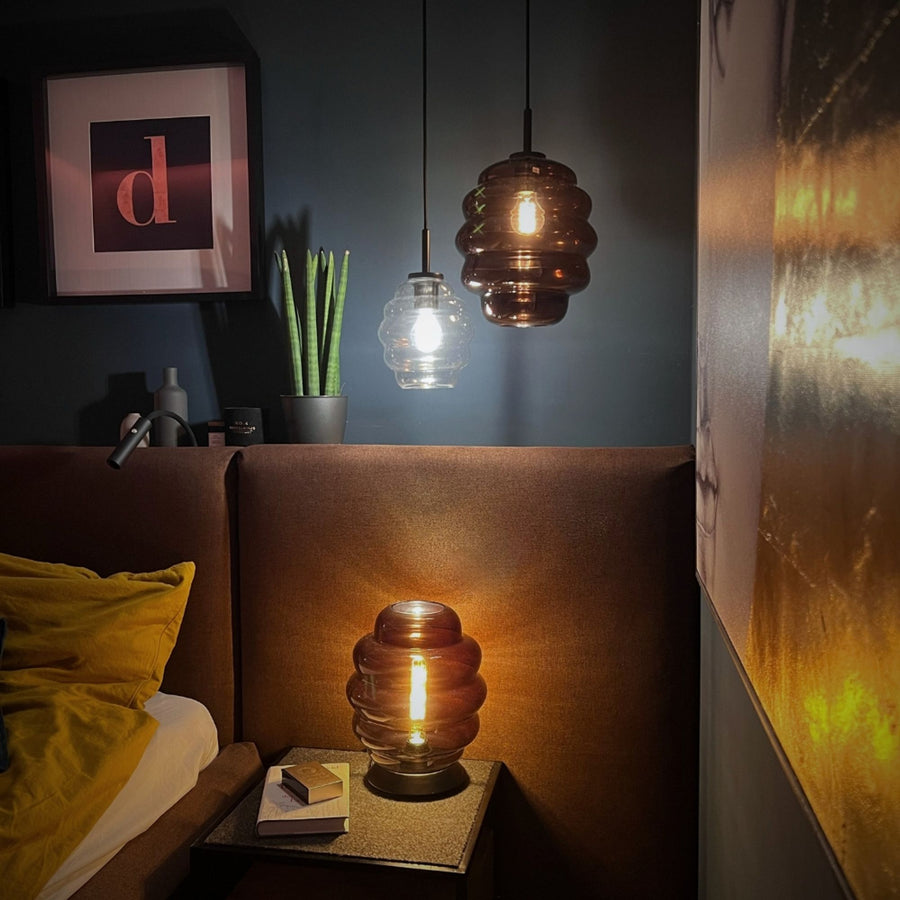 Lampe posée sur chevet de chambre, deux suspensions similaires visibles au-dessus