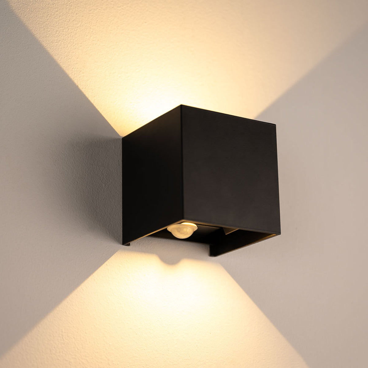 Applique cube noire allumée sur un mur, éclairage haut et bas