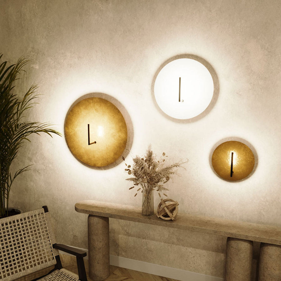 Trois appliques murales rondes LED dorées et blanches au-dessus d'un mobilier en béton