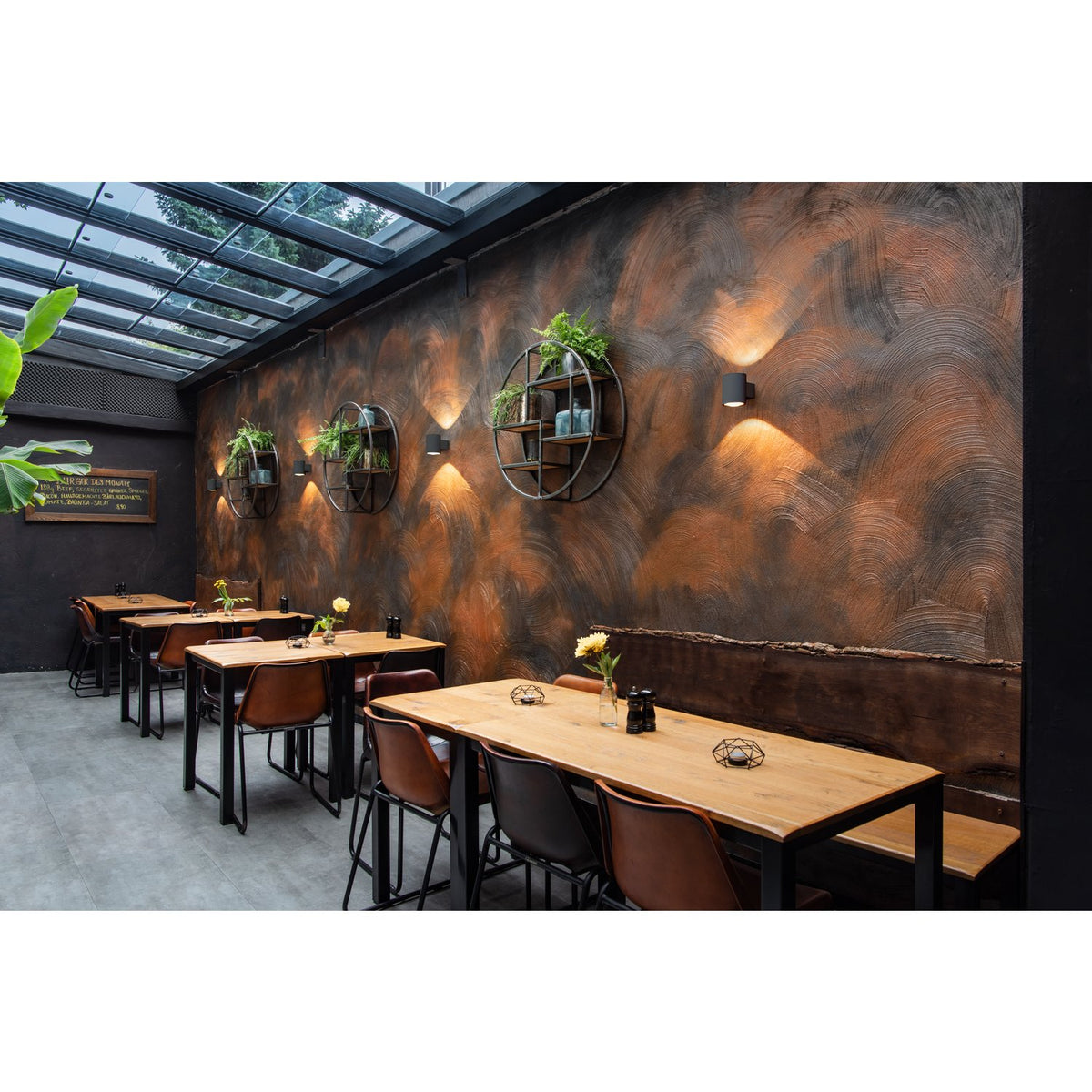 Ambiance de restaurant avec appliques murales noires éclairant un mur texturé.
