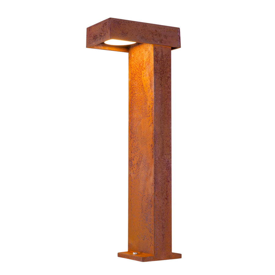 Lampadaire rouille de face, lumière allumée sous la tête et base au sol.