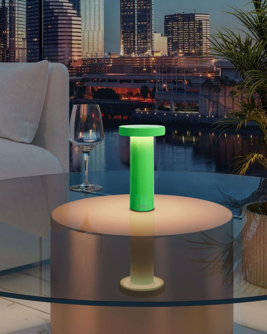 Lampe verte allumée posée sur table basse en terrasse urbaine au crépuscule