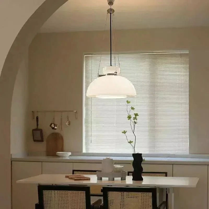 Suspension blanche devant une fenêtre à stores, au-dessus d'une table avec vase.