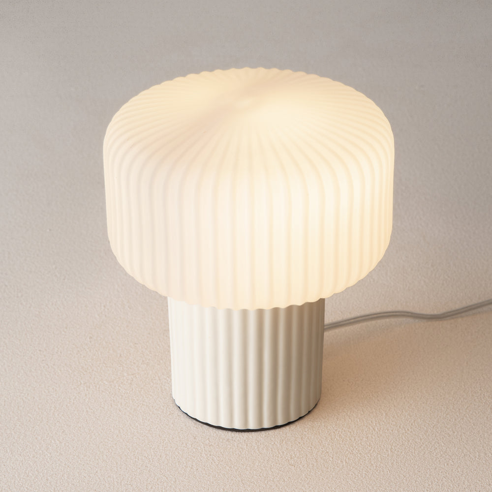 Vue en plongée de la lampe allumée, abat-jour strié et base cylindrique beige.