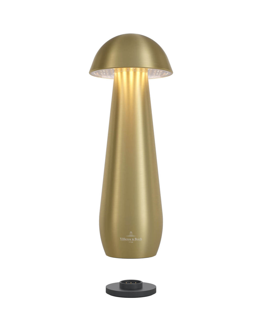 Lampe allumée sur sa base de recharge, lumière chaude sous le chapeau doré.