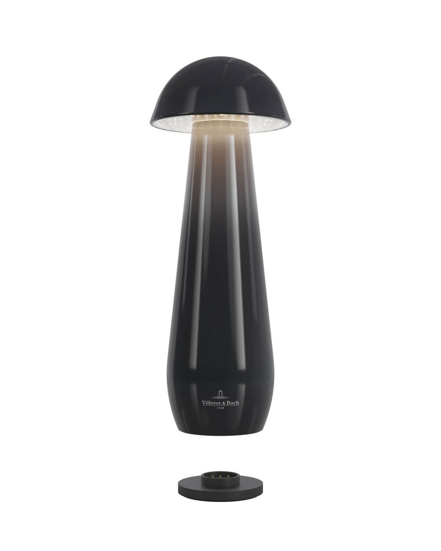 Luminaire allumé au-dessus de sa base de recharge noire, sur fond blanc.