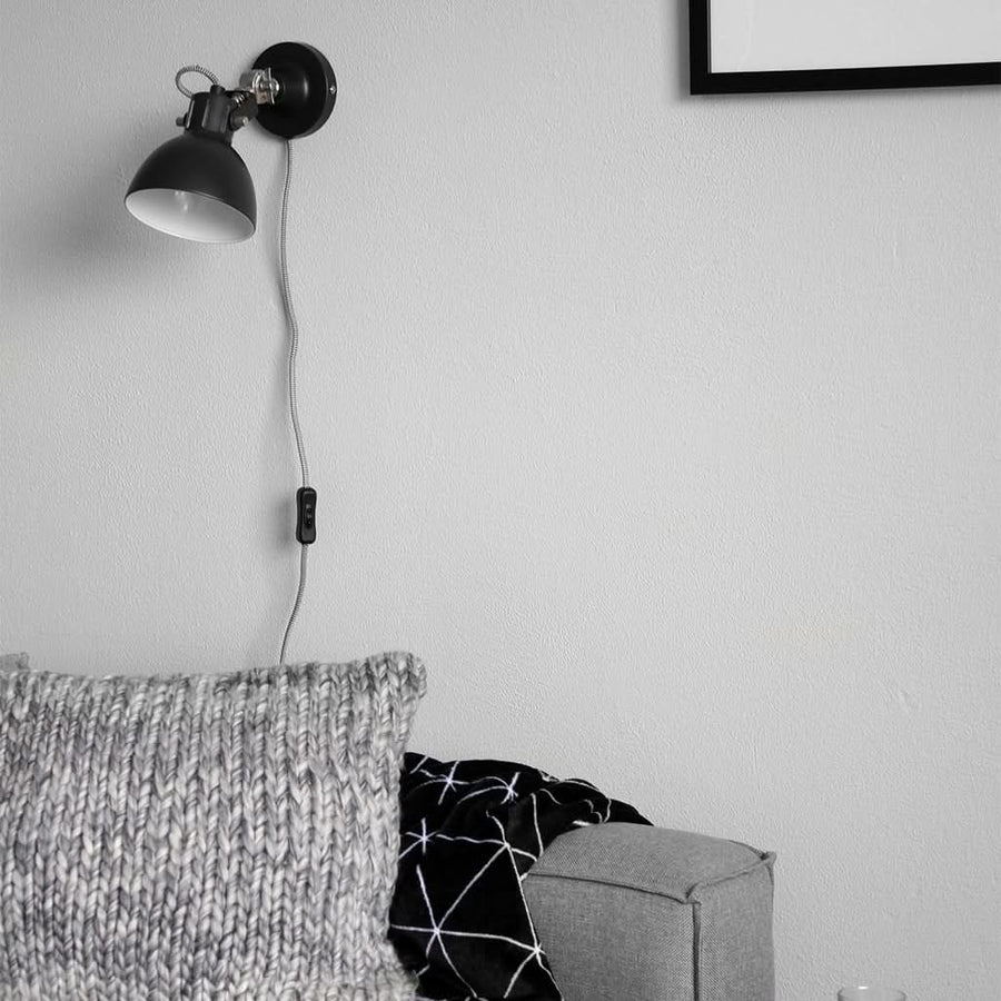 Applique murale noire avec cordon et interrupteur, canapé et coussin en arrière-plan