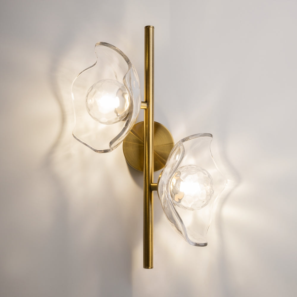 Applique murale dorée installée au mur, deux globes en verre transparent éclairés, ombres portées.