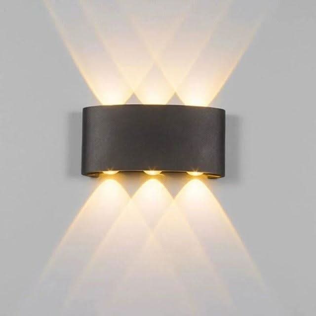 Gros plan d'une applique murale noire cylindrique, trois faisceaux lumineux vers le haut et le bas.