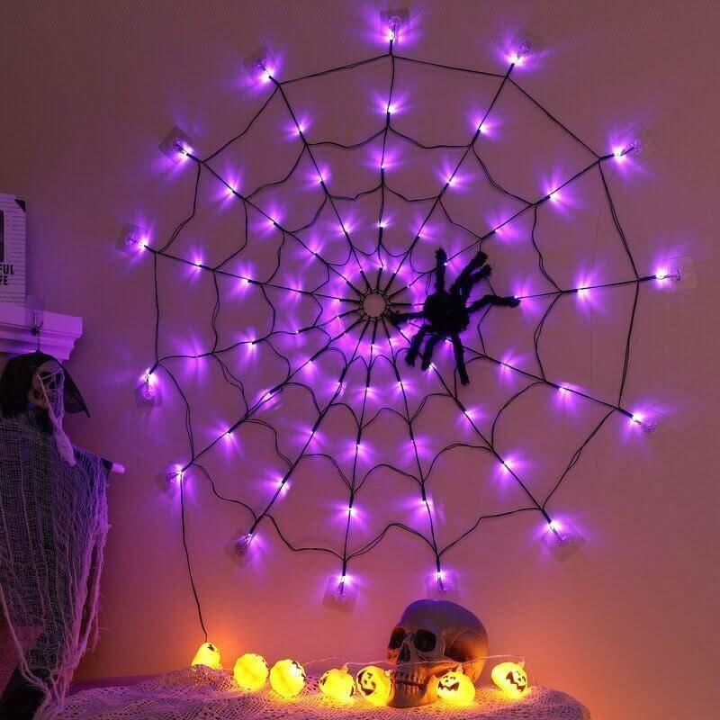 Toile d'araignée lumineuse violette accrochée au mur, araignée noire au centre, citrouilles éclairées dessous