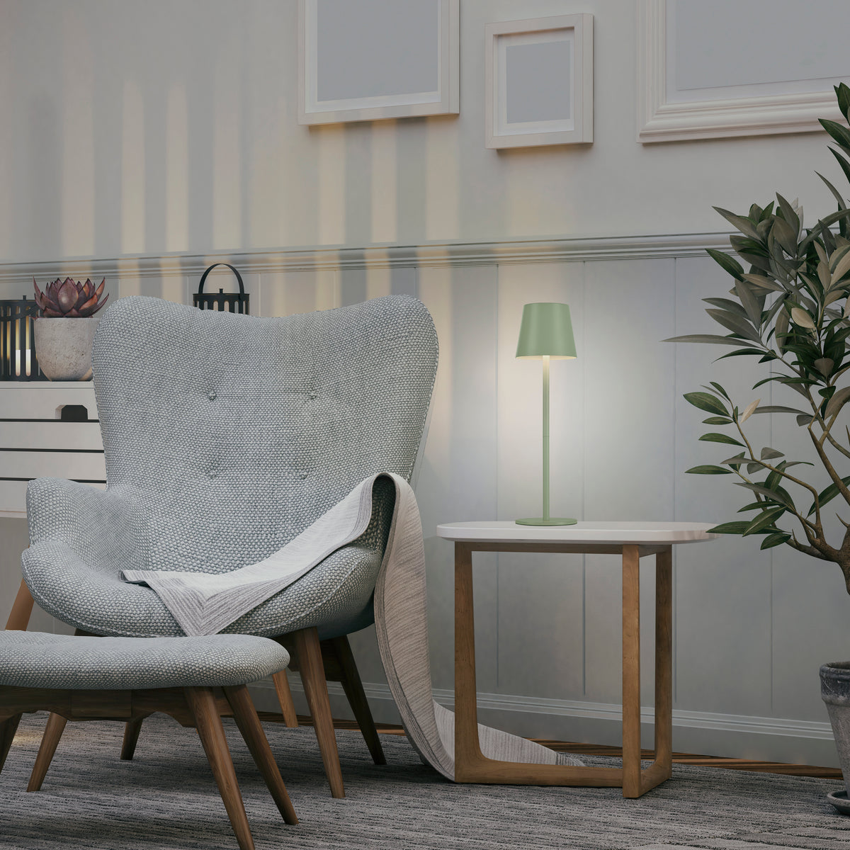 Mise en ambiance : lampe allumée sur table d'appoint près d'un fauteuil et d'une plante.