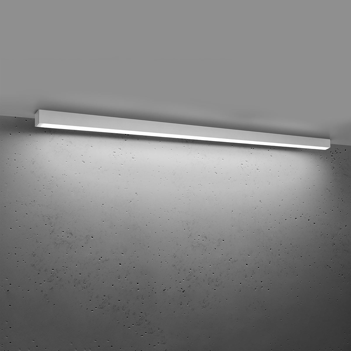 Luminaire allumé éclairant la pièce, lumière blanche projetée sur béton brut.