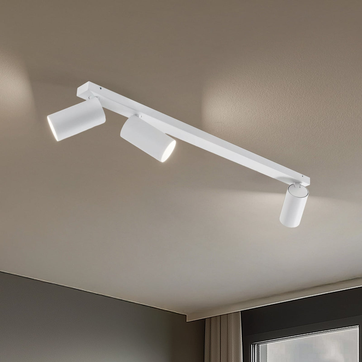 Vue rapprochée du luminaire blanc à trois spots cylindriques fixé au plafond, lumières allumées.