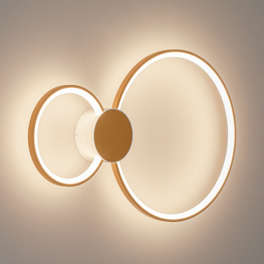 Applique murale LED double anneau allumée sur mur beige, vue de face