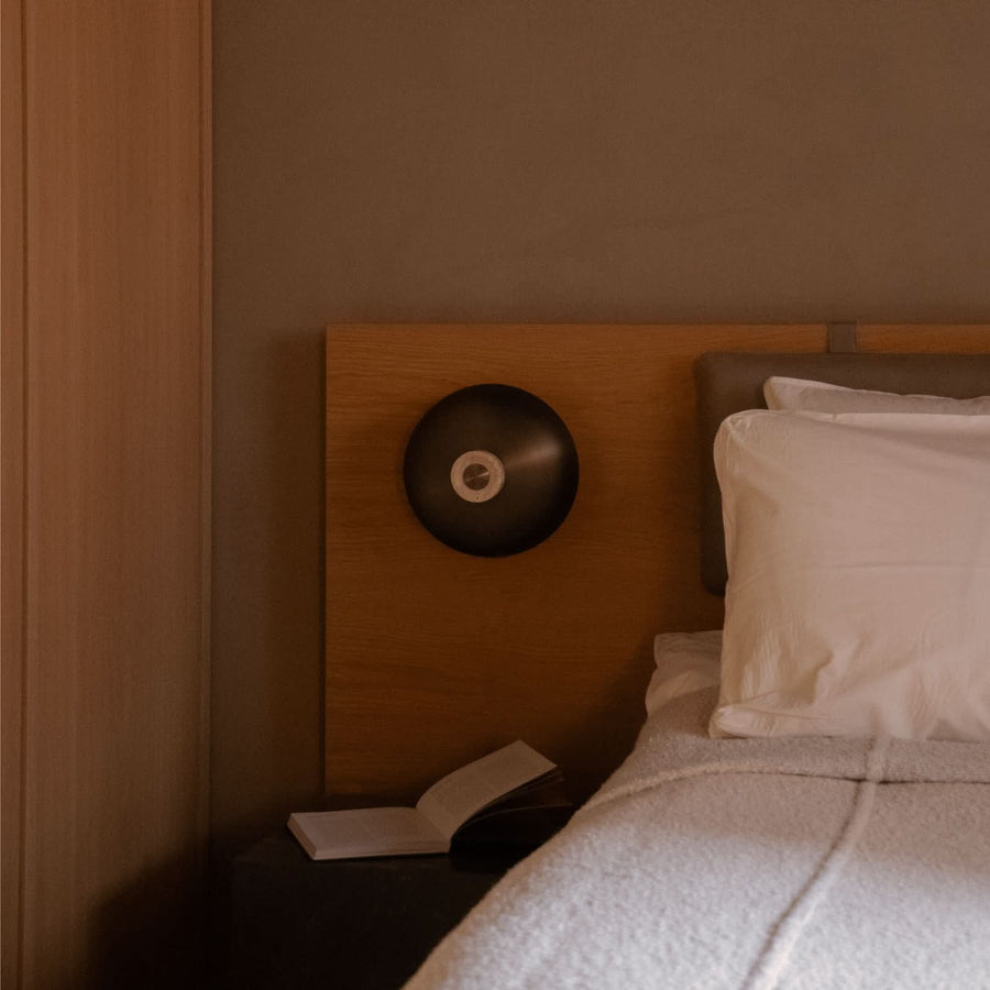Applique fixée sur une tête de lit en bois, livre ouvert à côté.