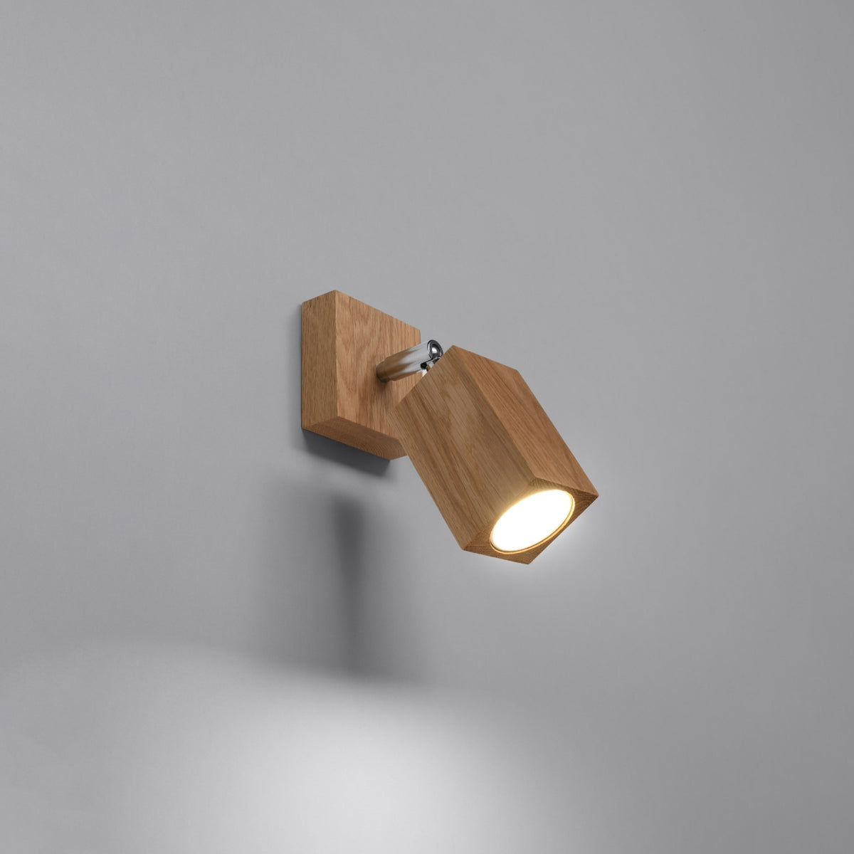 Version allumée de l'applique en chêne, diffusant une lumière chaude sur fond gris.