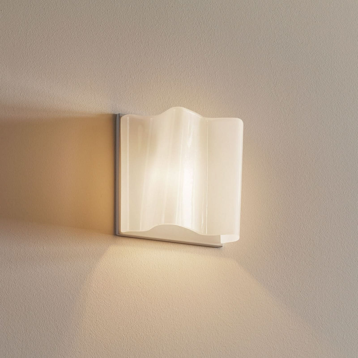 Applique murale blanche allumée sur un mur beige, lumière chaude diffuse.