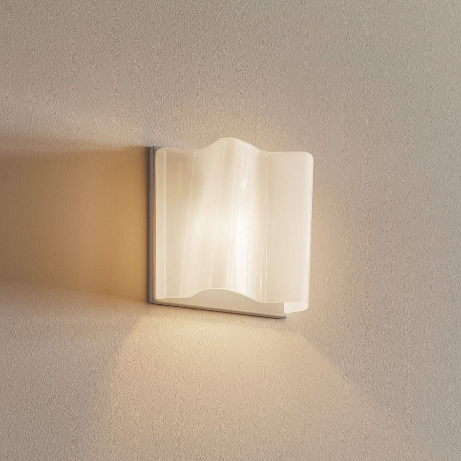 Applique murale blanche allumée sur un mur beige, lumière chaude diffuse.