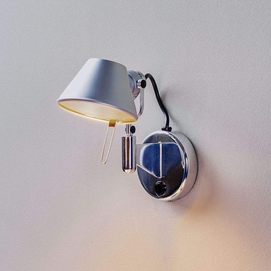 Applique murale chromée fixée au mur, abat-jour orienté vers le bas et lumière chaude.