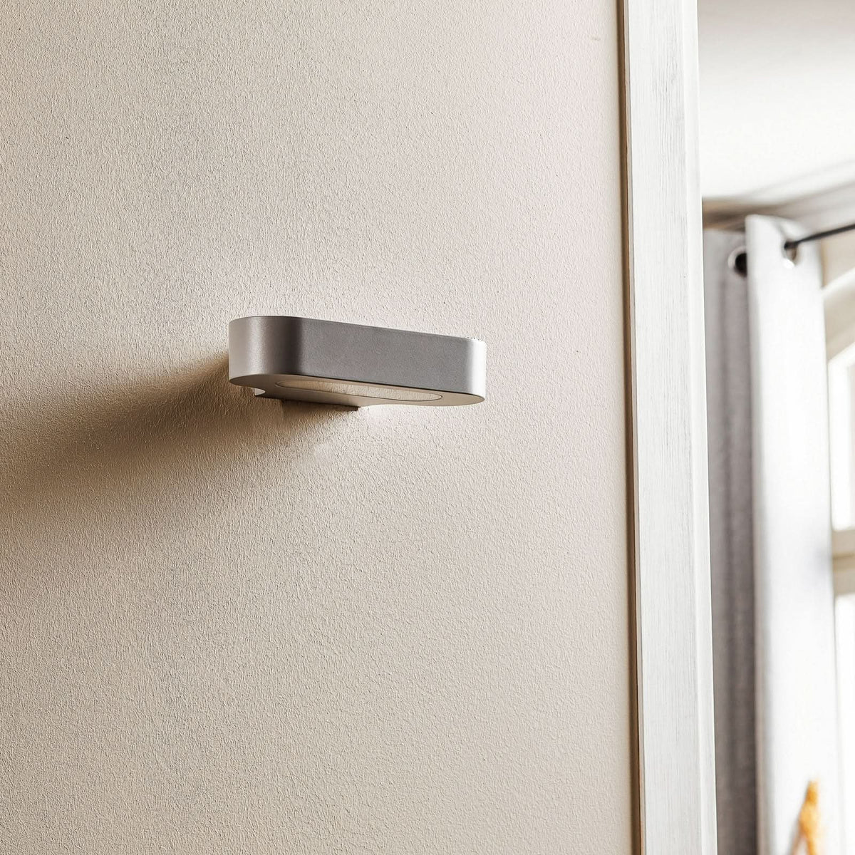 Vue rapprochée de l'applique éteinte sur mur beige, finition argent.