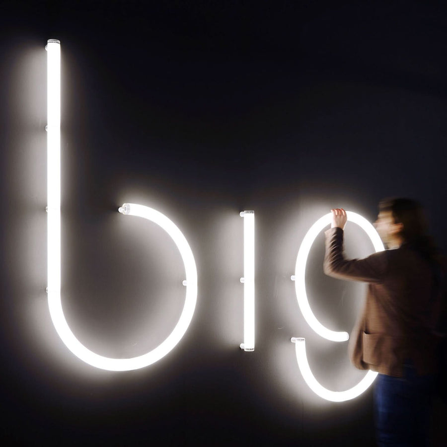 Personne ajustant des lettres lumineuses blanches sur un mur noir.